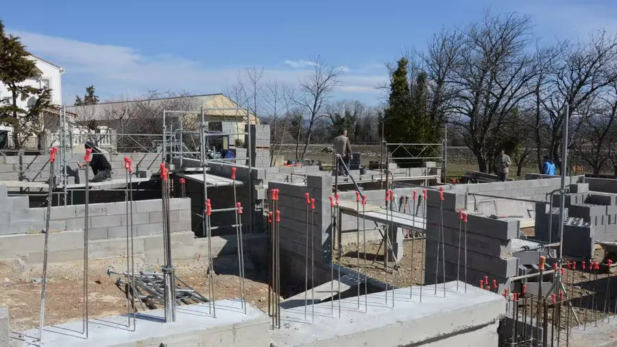 Sunlit construction site with workers on concrete foundation under a clear blue sky.