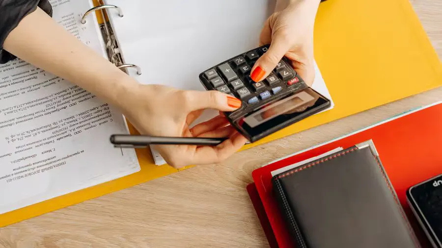 Hands using a calculator at a desk with documents and folders, ideal for finance or accounting themes.